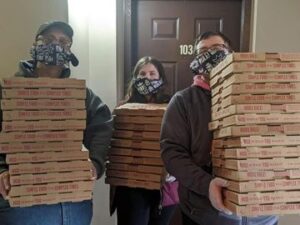 Three people holding 30 pizzas.